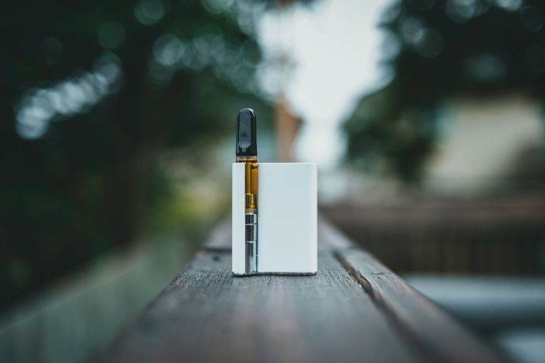 Sleek cannabis vape pen resting on a wooden surface outdoors in natural light
