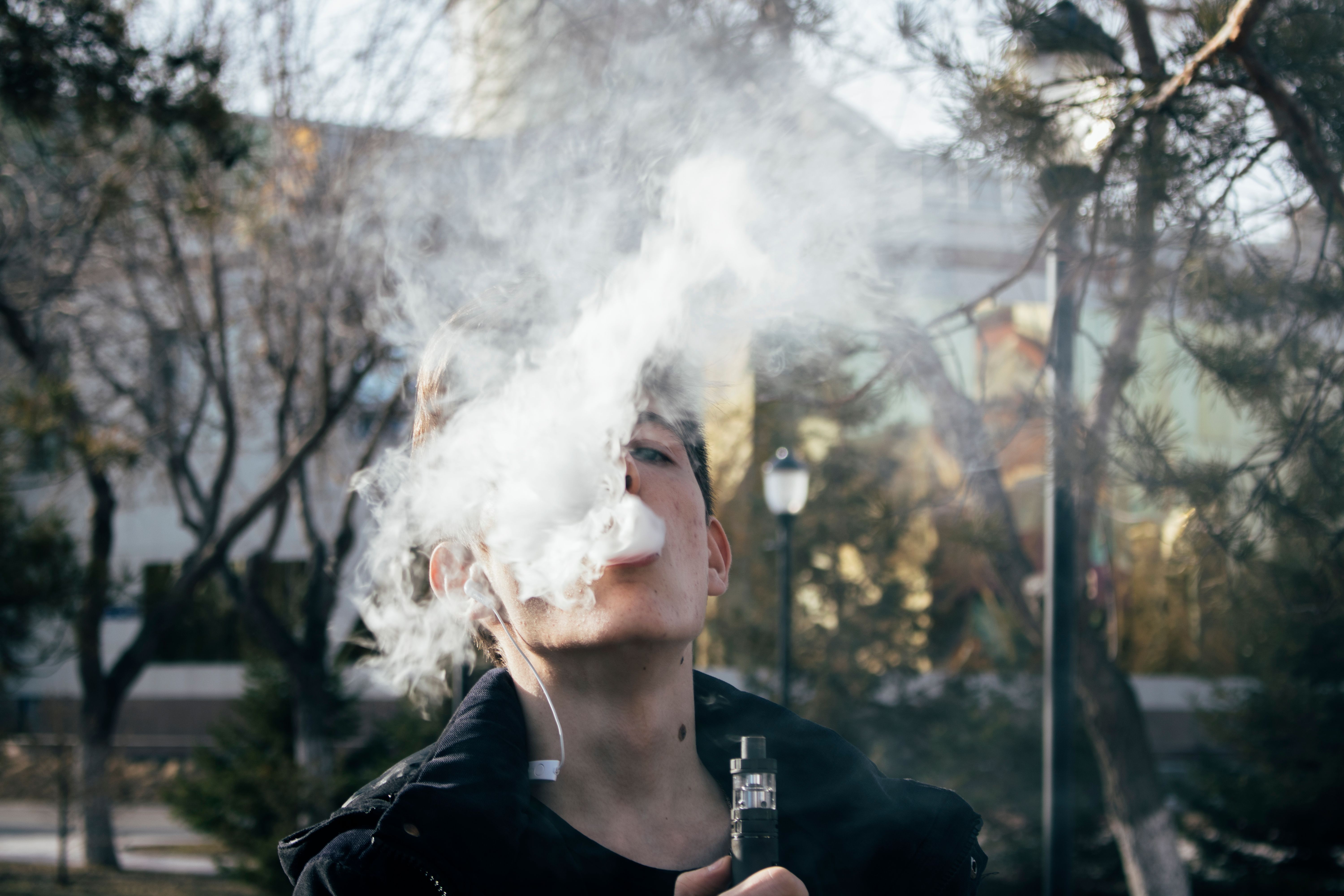 Person exhaling a thick dense vapor cloud from a vape on a clear day